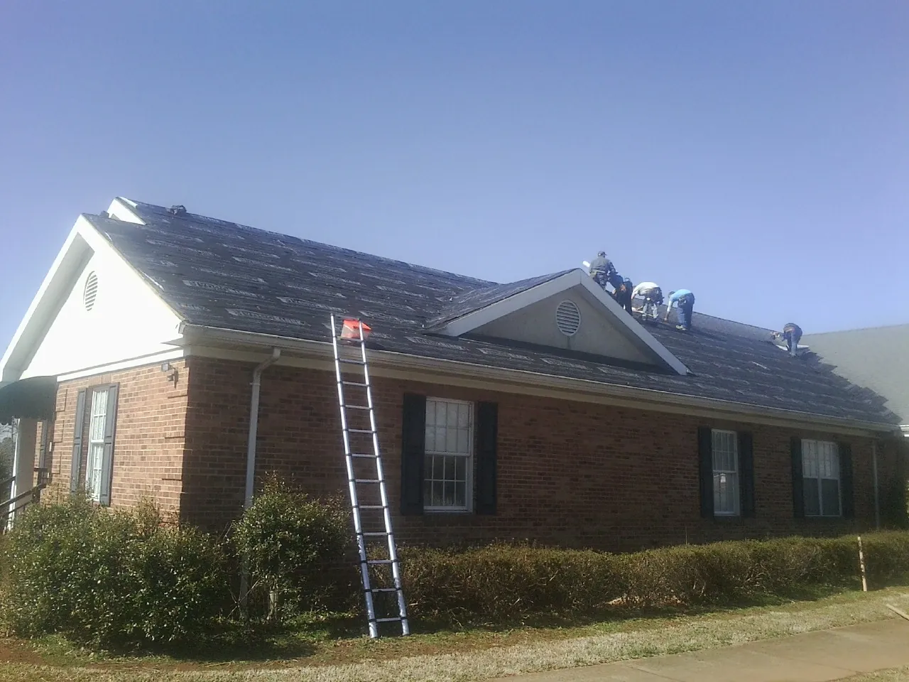 Crew tearing shingles off a brick ranch roof with a ladder set — Metal Roof Repair work by our crew in Plymouth